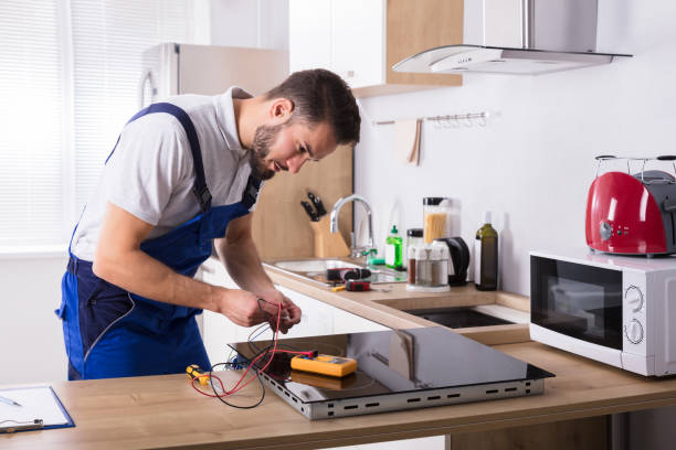 Male Technician Repairing Induction Stove With Digital Multimeter In Kitchen
